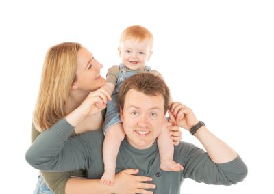 Young, smiling baby piggybacking his dad whilst mum looks on laughing Wirral family photographer