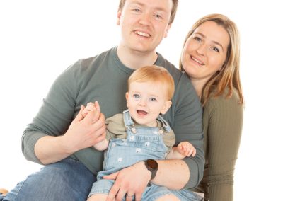 Father sitting down holding smiling baby together with mother Wirral family photographer