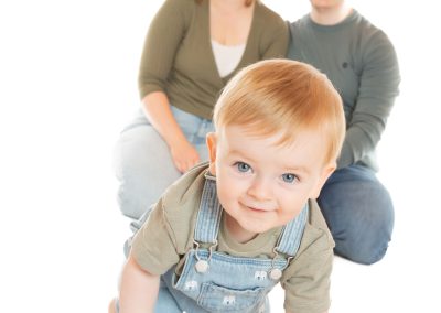 Parents sitting behind a baby crawling towards the camera and smiling Wirral family photographer