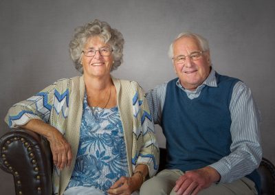 Grandparents sitting down dressed in blue and grey clothing smiling at the camera.