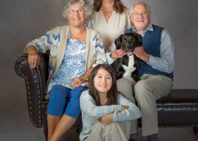 Grandparents sitting on a chaise with a black doodle dog together with their sitting granddaughter Wirral family Photogrpaher