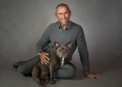 Man sitting down on floor stroking his French Bulldog and smiling