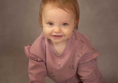 Small baby in a prirple outfit, smiling and crawling towards the camersa Wirral children's photographer