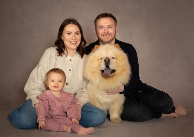 Mum and dad together with 1 year old baby and Chow Chow dog sitting on the floor smiling at camera Wirral pet photographer