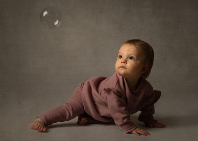 Gorgeous baby lying on the floor looking up at a floating bubble in wonderment