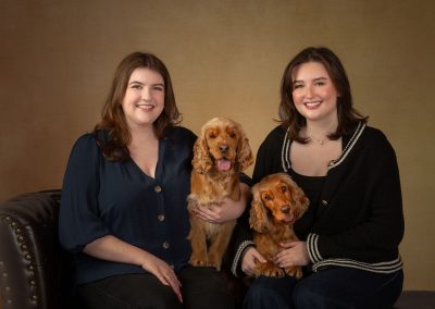 2 beautiful red cocker spaniels sitting on a chaise long inbetween 2 sisters Wirral family photographer