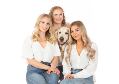 3 young sisters in white blouses and jeans sitting down and surrounding their white retriever Wirral family photographer