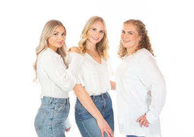 3 young sisters standing up in white blouses and jeans smiling Wirral family photographer